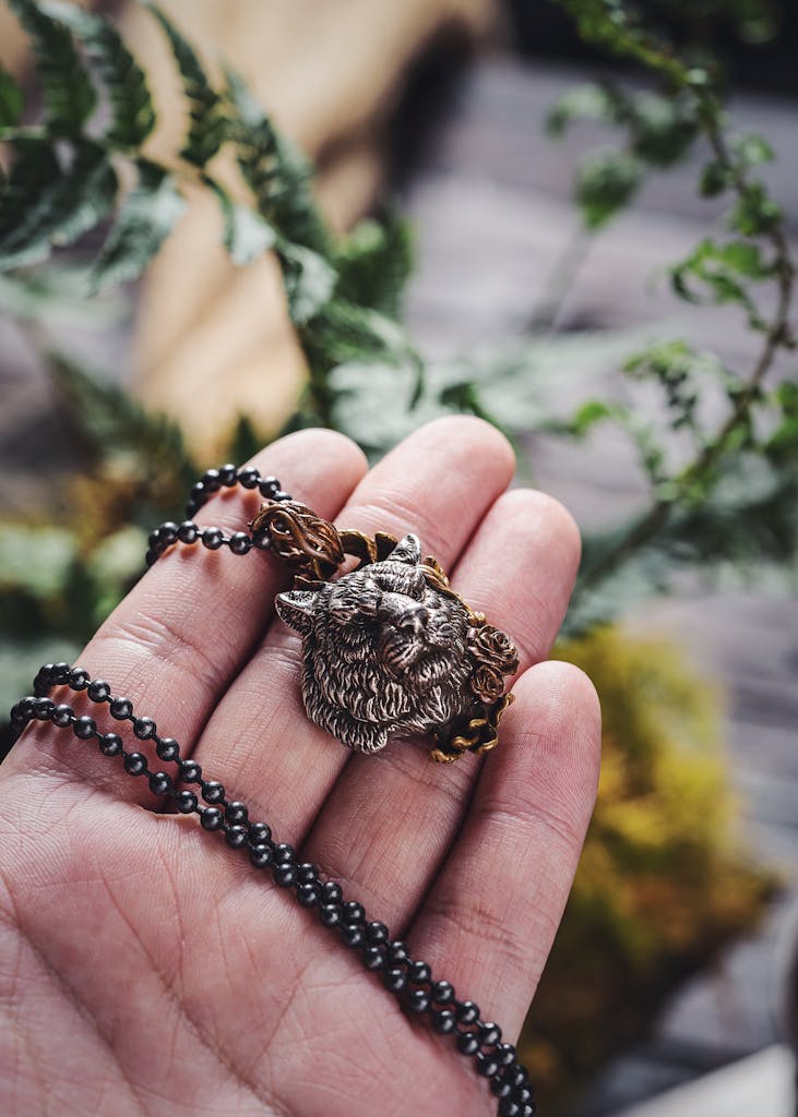 Close-up of a hand holding an intricate tiger pendant with background foliage.