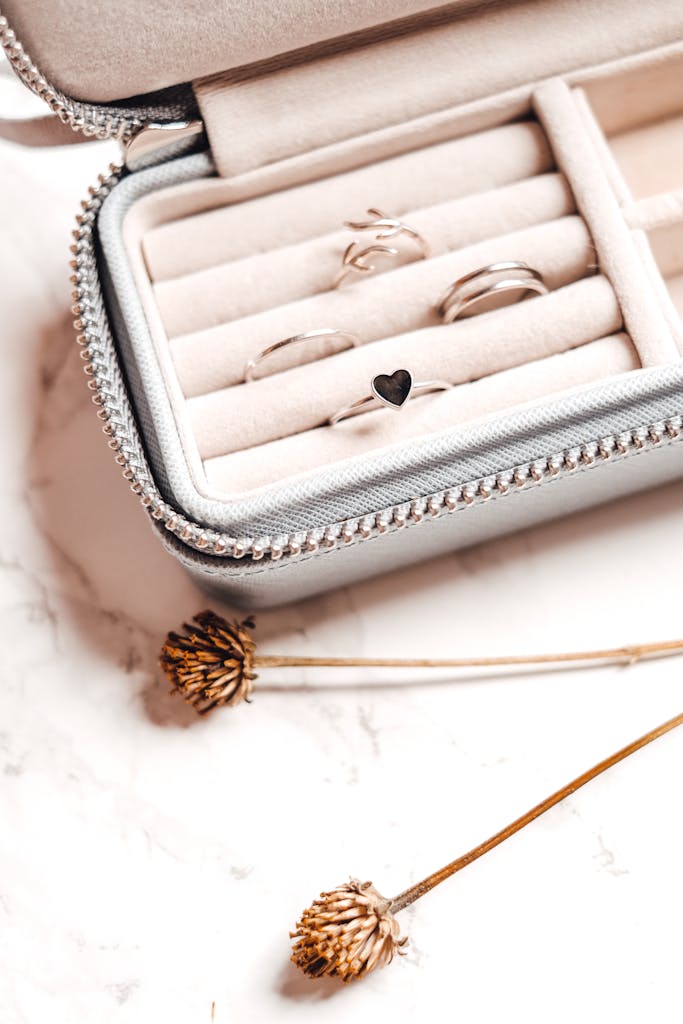 Close-up of silver rings in an organizer on marble surface with dried flowers.